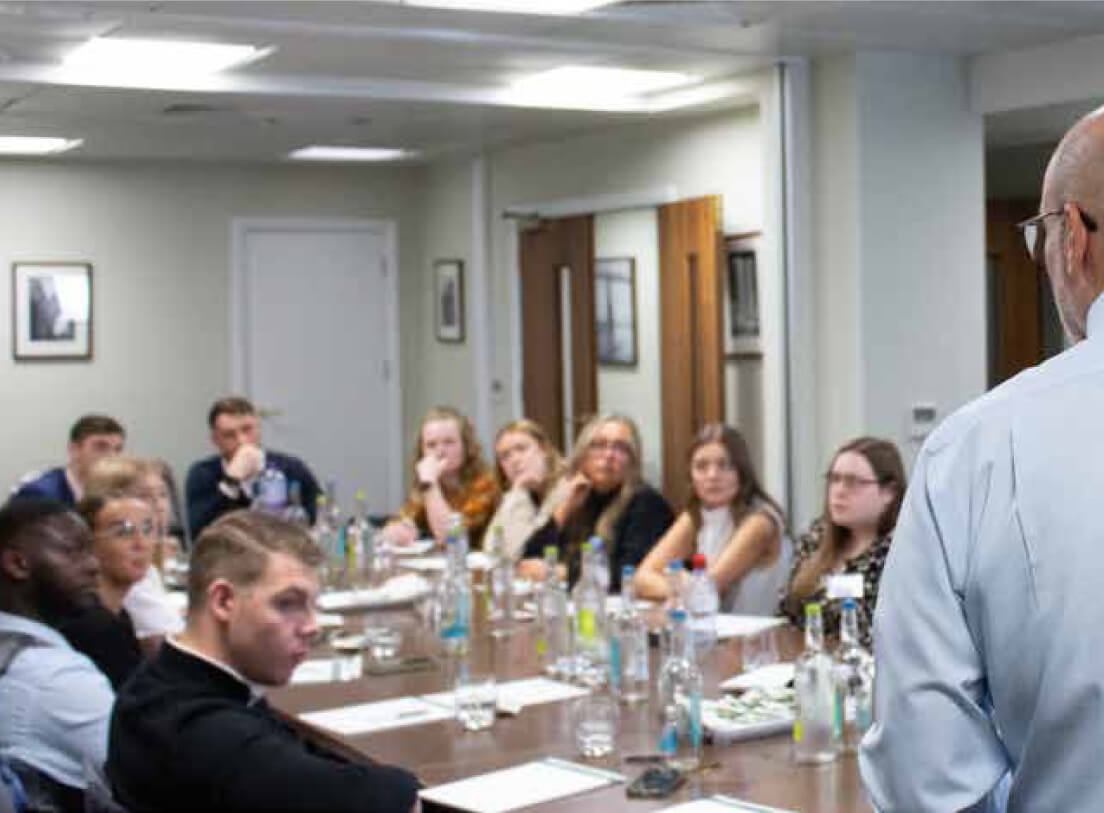Don stands in front of clerks at a table, delivering a presentation and actively engaging his audience.